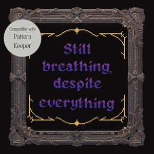 Op de afbeelding: Kruissteekontwerp met de woorden "Still breathing, despite everything" in paars op een zwarte achtergrond. Het ontwerp is omlijst in een decoratieve, sierlijke bruine lijst met gouden accenten. Een witte cirkel met tekst staat linksboven.