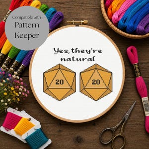 Può includere: Un telaio da ricamo rotondo in legno contenente un disegno a punto croce su tessuto bianco. Il design presenta due dadi gialli a venti facce con il numero 20 visibile su ciascuno e il testo nero Yes, they're natural centrato sopra.