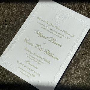May include: A formal wedding invitation on white cardstock with embossed floral and scroll details. The text is in a soft green, announcing the marriage of Abigail Lauren to Cason Cole Whitmire. The invitation includes the date, time, and location.
