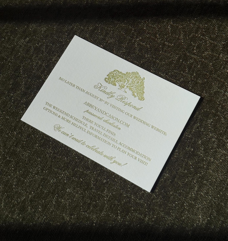 Puede incluir: Una tarjeta de invitaci&oacute;n de boda blanca con texto dorado y una ilustraci&oacute;n de &aacute;rbol. El texto incluye "Kindly Respond", una direcci&oacute;n web y otros detalles de la boda. La tarjeta est&aacute; sobre una superficie oscura y texturizada.