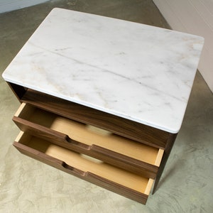 May include: A walnut wood bedside table with two drawers and a white marble top.