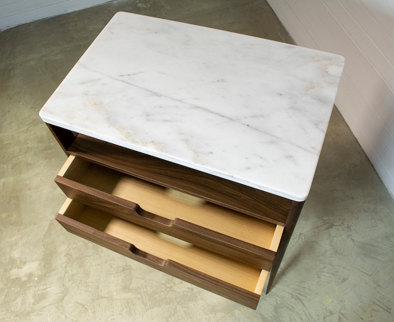 May include: A walnut wood bedside table with two drawers and a white marble top.