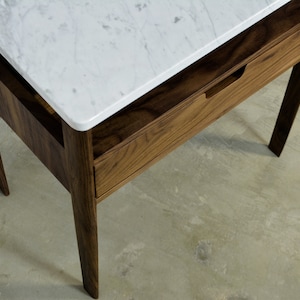 May include: A wooden nightstand with a white marble top and a single drawer. The nightstand has a simple design with straight lines and a dark wood finish.