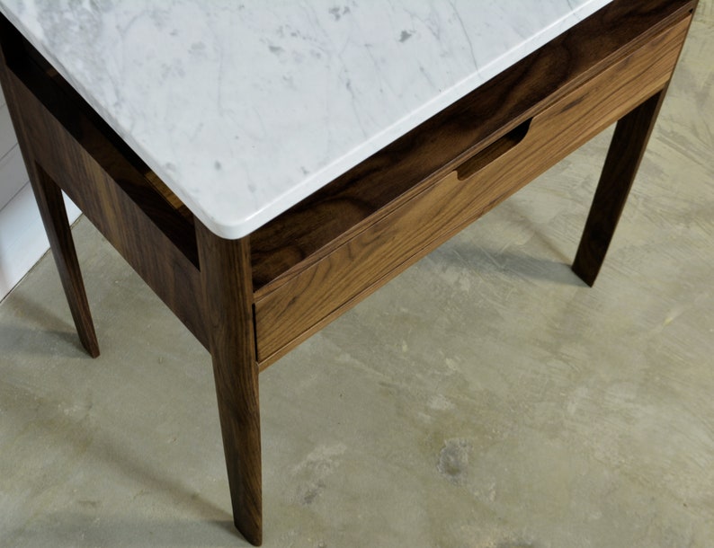 May include: A wooden nightstand with a white marble top and a single drawer. The nightstand has a simple design with straight lines and a dark wood finish.