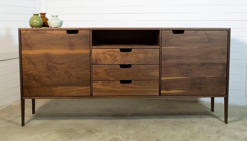 Puede incluir: Un aparador de madera de nogal con cuatro cajones y dos puertas. El aparador tiene un dise&ntilde;o moderno con patas de metal negro y un aspecto simple y limpio.