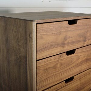 May include: A tall wooden dresser with five drawers. The dresser is made of a light brown wood with a natural finish. The drawers have simple, recessed handles.