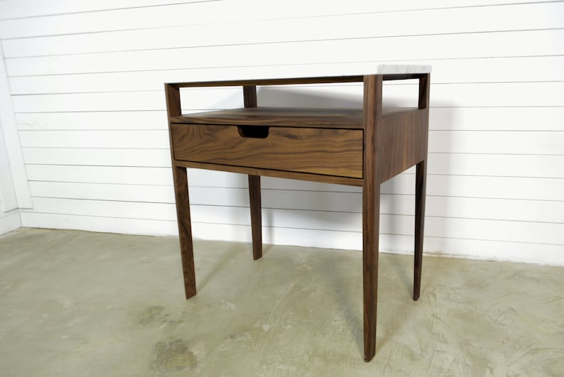 May include: A walnut wood end table with a single drawer and a shelf. The table has a modern design with clean lines and a simple, elegant look.