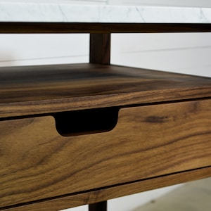 May include: A wooden end table with a white marble top and a single drawer. The drawer has a recessed handle.