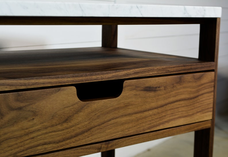 May include: A wooden end table with a white marble top and a single drawer. The drawer has a recessed handle.