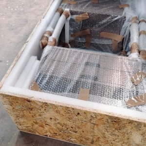 May include: A wooden crate containing a brown cardboard box. The box is wrapped in bubble wrap and secured with brown tape.