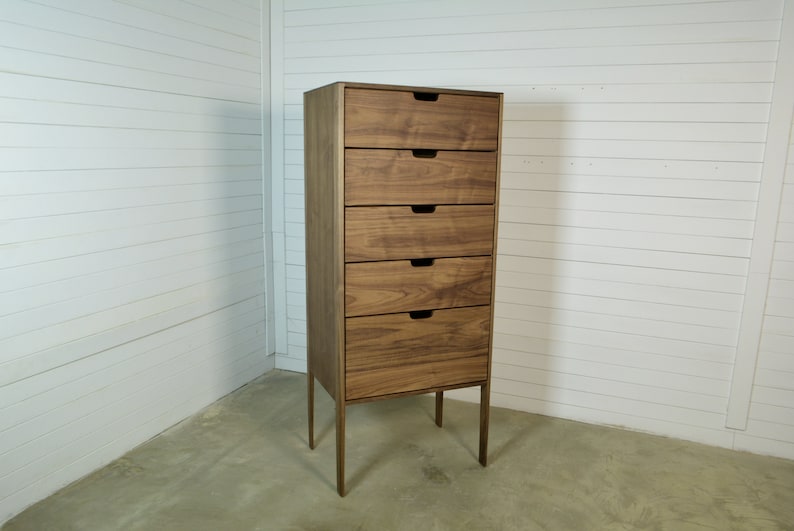 May include: A tall wooden dresser with five drawers and a light brown finish. The dresser has a simple design with metal legs.
