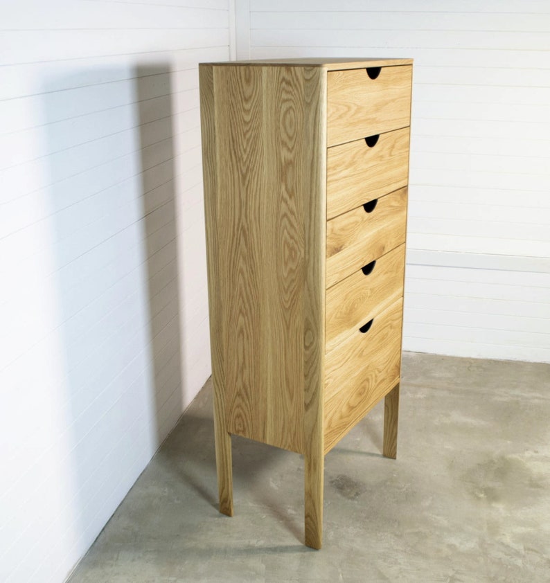 May include: A tall wooden chest of drawers with six drawers and black handles. The dresser has a light wood finish and stands on four legs.