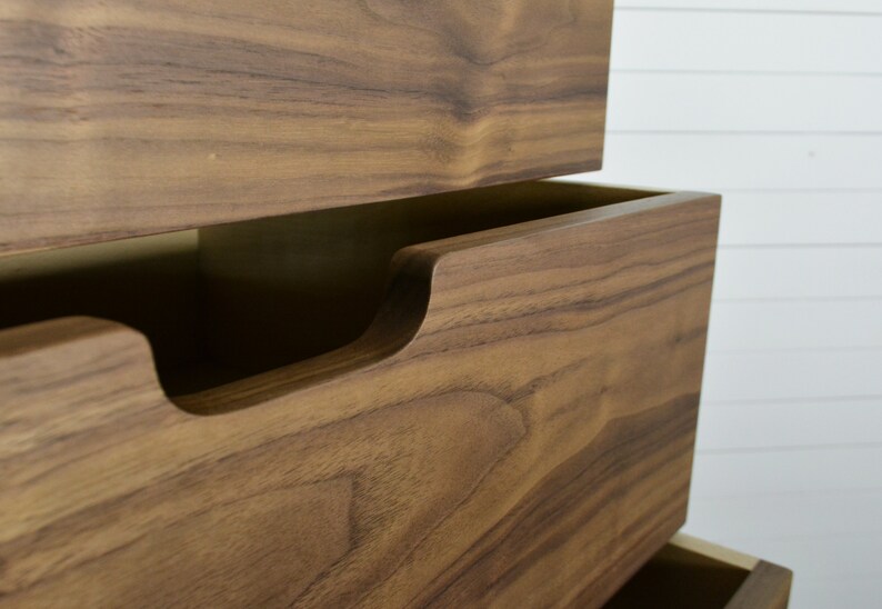 May include: Close-up of a wooden dresser drawer with a recessed handle. The drawer is made of a rich brown wood with a natural grain pattern.