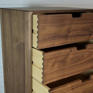 May include: A tall wooden dresser with four drawers. The drawers are made of a light brown wood and have a slightly darker brown finish. The dresser is made of a darker brown wood and has a smooth finish.