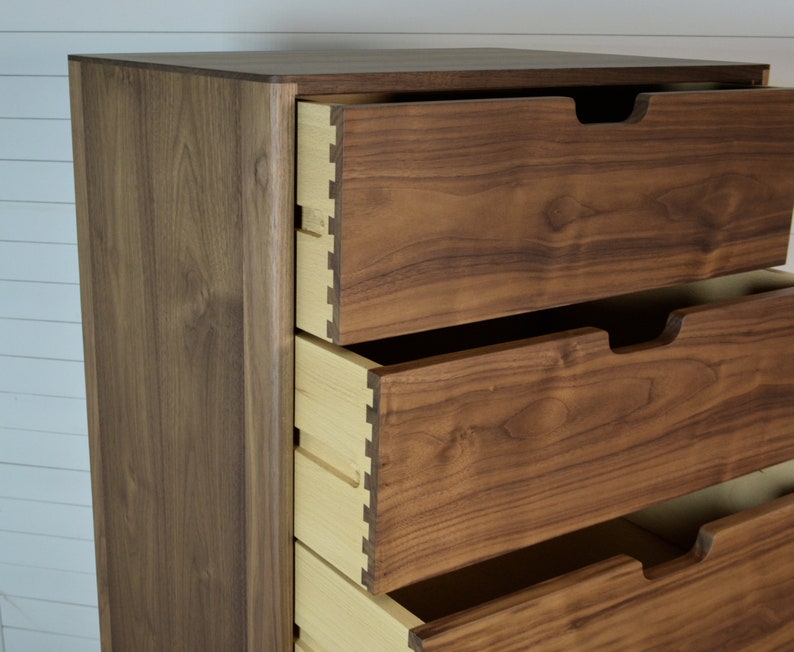 May include: A tall wooden dresser with four drawers. The drawers are made of a light brown wood and have a slightly darker brown finish. The dresser is made of a darker brown wood and has a smooth finish.
