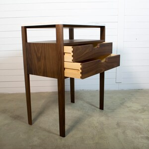 May include: A two-drawer bedside table with a walnut wood frame and a white marble top. The drawers are open, revealing a light wood interior.