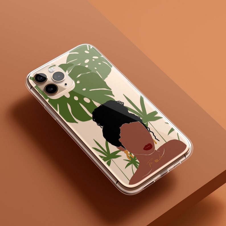 May include: A clear phone case with a design of a woman with dark skin and a bun, surrounded by green tropical leaves. The case is compatible with an iPhone.