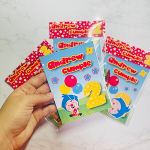 May include: A stack of colourful personalised colouring books with the name "Andrew cumple" and the number "2" on the front. The books feature a cartoon clown with balloons and stars.