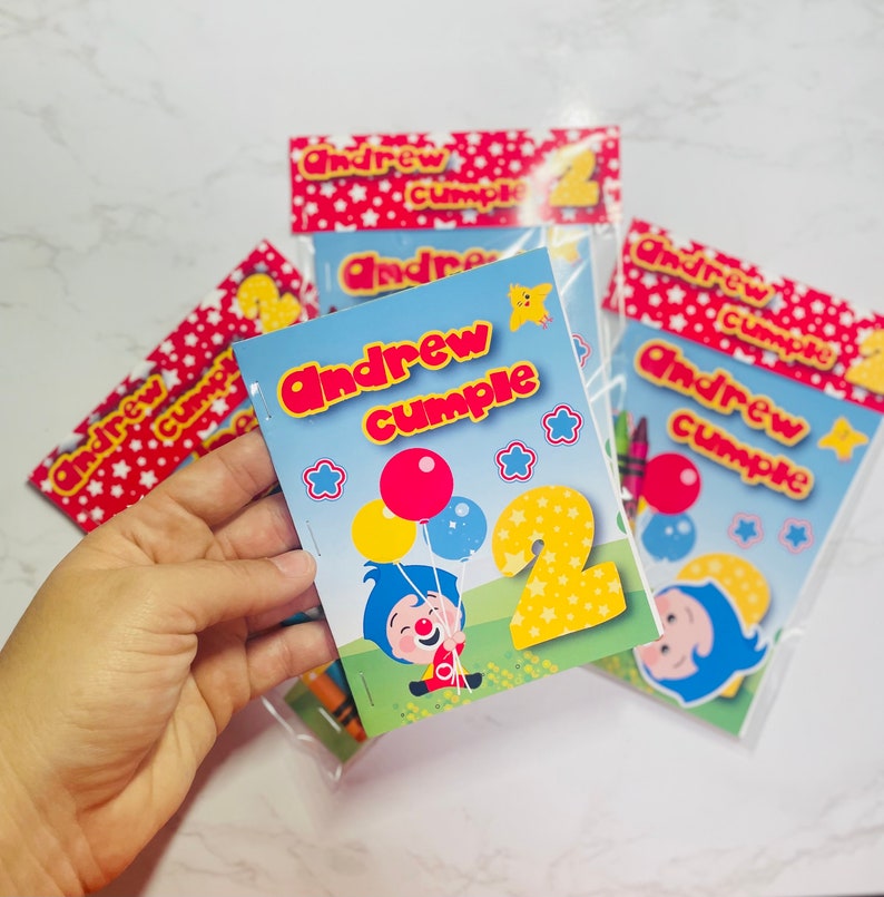May include: A stack of colourful personalised colouring books with the name "Andrew cumple" and the number "2" on the front. The books feature a cartoon clown with balloons and stars.