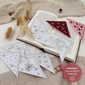 May include: A collection of printable stick and stitch templates, including triangular designs with bee, butterfly, cherry, and floral patterns. Two felt pennants with bow designs are also visible. The templates are displayed on an open book.