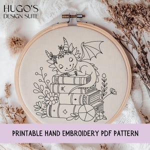 May include: A hand embroidery pattern featuring a sleeping dragon on a stack of books, framed in a wooden hoop. The design is outlined in black on a beige fabric. The text "PRINTABLE HAND EMBROIDERY PDF PATTERN" is at the bottom.