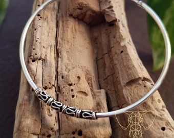 May include: Two silver hoop earrings with a decorative design around the edge. The earrings are on a wooden surface.