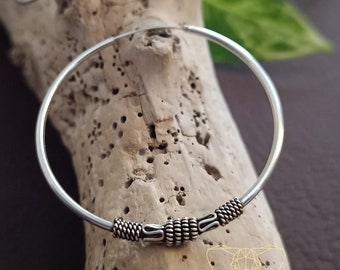 May include: Silver hoop earrings with a braided design. The earrings are on a wooden surface.