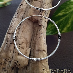 May include: Two silver hoop earrings with decorative accents. The earrings are on a wooden surface.