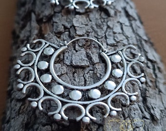 May include: A pair of silver hoop earrings with a decorative design. The earrings are made of metal and have a circular shape. The design features a series of small circles and curves.