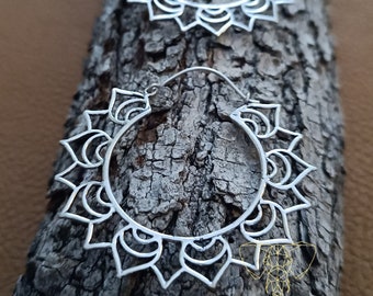 May include: Two silver hoop earrings with a mandala design. The earrings are made of metal and have a delicate, intricate pattern.