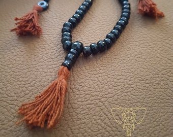 May include: Black beaded mala necklace with brown tassels. The necklace is made of black beads and has a tassel at each end. The tassels are made of brown string and are about 1 inch long.