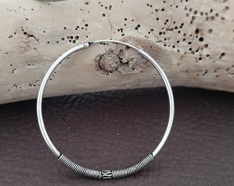May include: A pair of silver hoop earrings. The lower portion of each earring is wrapped with a coiled wire design. The earrings are displayed on a brown surface.