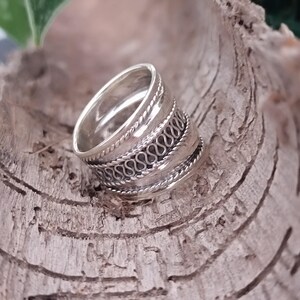 May include: A silver ring with a wide band and intricate woven designs. The ring is made of sterling silver and has a polished finish.