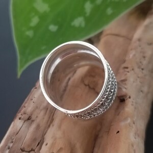 May include: Silver ring with a detailed woven design. The ring is thick and has a rounded band.