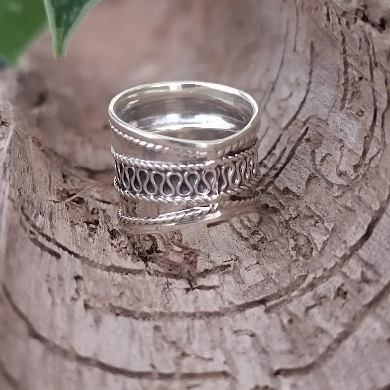 May include: A silver ring with a wide band and intricate woven detailing. The ring is made of sterling silver and has a polished finish.