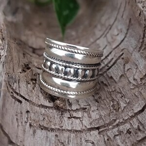 May include: A silver ring with a wide band and multiple rows of decorative beading.