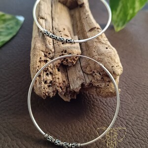 May include: Two silver hoop earrings with decorative accents. The hoops are on a wooden surface.
