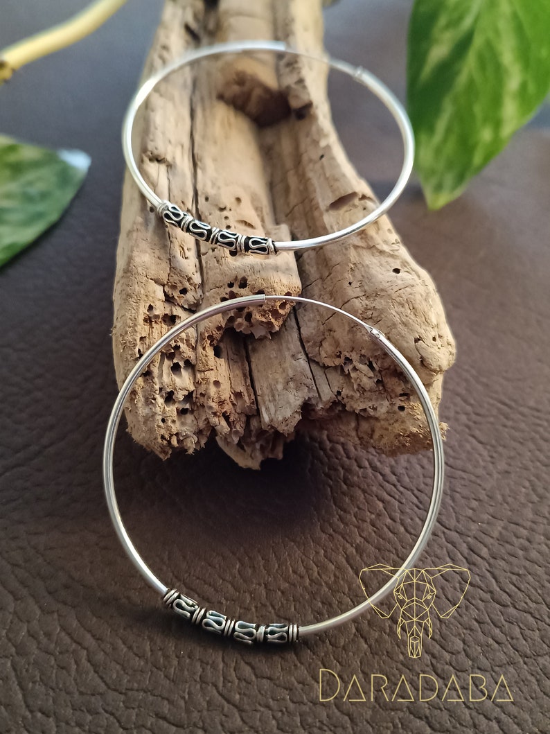 May include: Two silver hoop earrings with decorative accents. The hoops are on a wooden surface.