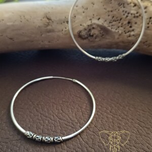 May include: A pair of silver hoop earrings with a decorative design. The hoops are large and have a simple, elegant look.