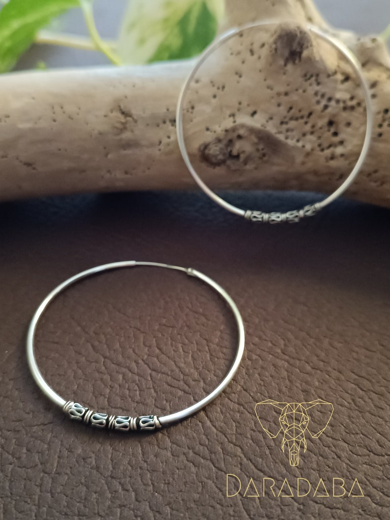 May include: A pair of silver hoop earrings with a decorative design. The hoops are large and have a simple, elegant look.