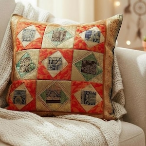 Könnte beinhalten: Ein dekoratives Zierkissen mit einem Patchwork-Design in Rot-, Orange-, Grün- und Goldtönen. Das Kissen liegt auf einem cremefarbenen Sofa und ist mit einer Strickdecke bedeckt. Das Design des Kissens zeigt geometrische Formen.