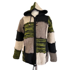 Peut inclure: Veste à capuche patchwork avec fermeture éclair. La veste présente des couleurs variées : noir, vert olive, beige et marron. La capuche est rayée. La veste a deux poches et un cordon de serrage en bas.