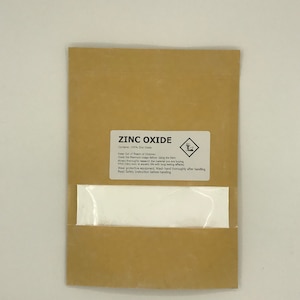 May include: A brown paper bag with a white label that reads "ZINC OXIDE" and contains 100% Zinc Oxide. The label also includes a warning symbol and instructions for safe handling.