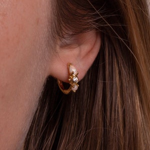 May include: Gold hoop earrings with small white pearl accents and a single clear rhinestone in the center.