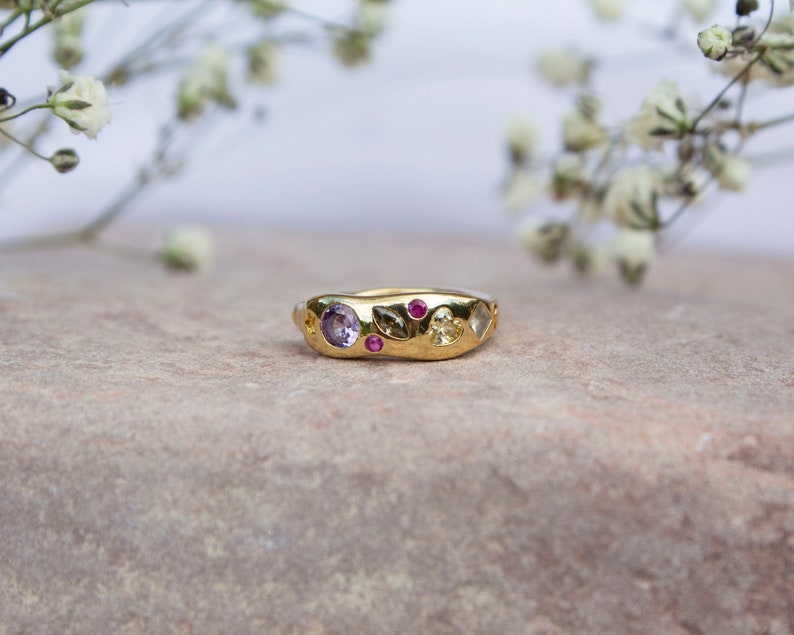 Pode incluir: Um anel de ouro com uma banda texturizada e v&aacute;rias pedras preciosas coloridas. O anel apresenta uma ametista roxa, rubis rosa e uma citrina amarela.
