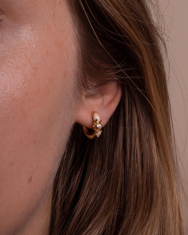 May include: Gold hoop earrings with small white pearl accents and a single clear rhinestone in the center.