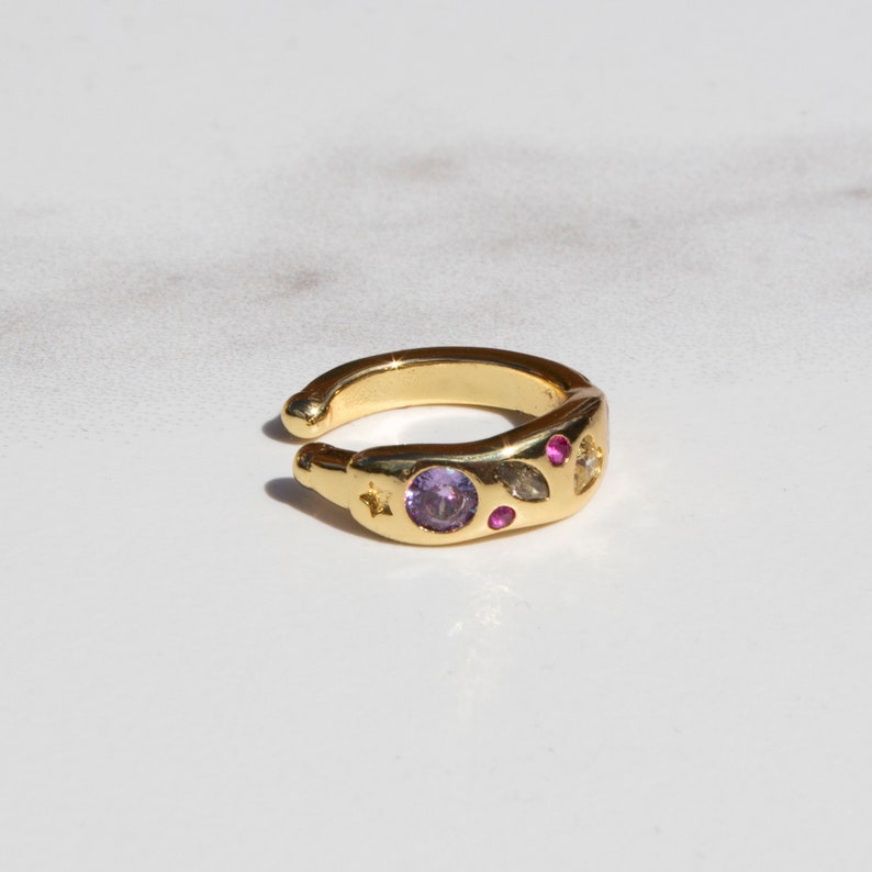 Pode incluir: Brinco de orelha dourado com um design de pedras preciosas roxas e rosas. O brinco tem um design de estrela e folha.