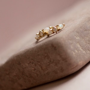 May include: A delicate gold ring with a row of small white opals and clear gemstones.