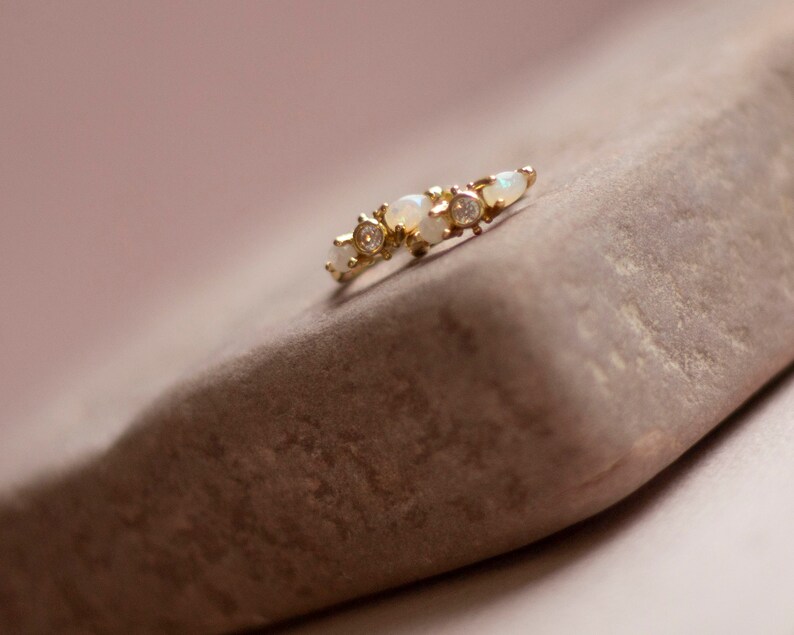May include: A delicate gold ring with a row of small white opals and clear gemstones.