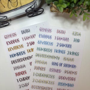 May include: Two sheets of stickers with Bible book names in various colors. The stickers include names like Genesis, Exodus, and Leviticus. The text is in a handwritten style, with each word in a different color.